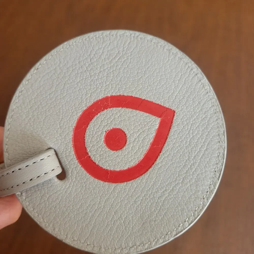 Round textured leather luggage tag in light grey with a red map